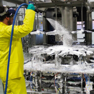 Worker applying an alkaline foam cleaner to stainless steel tanks, achieving high sanitation standards.